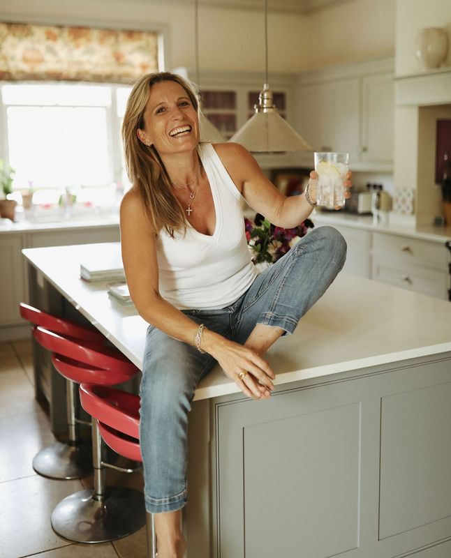 Woman sitting on a kitchen island, smiling in a bright white kitchen with red stools.