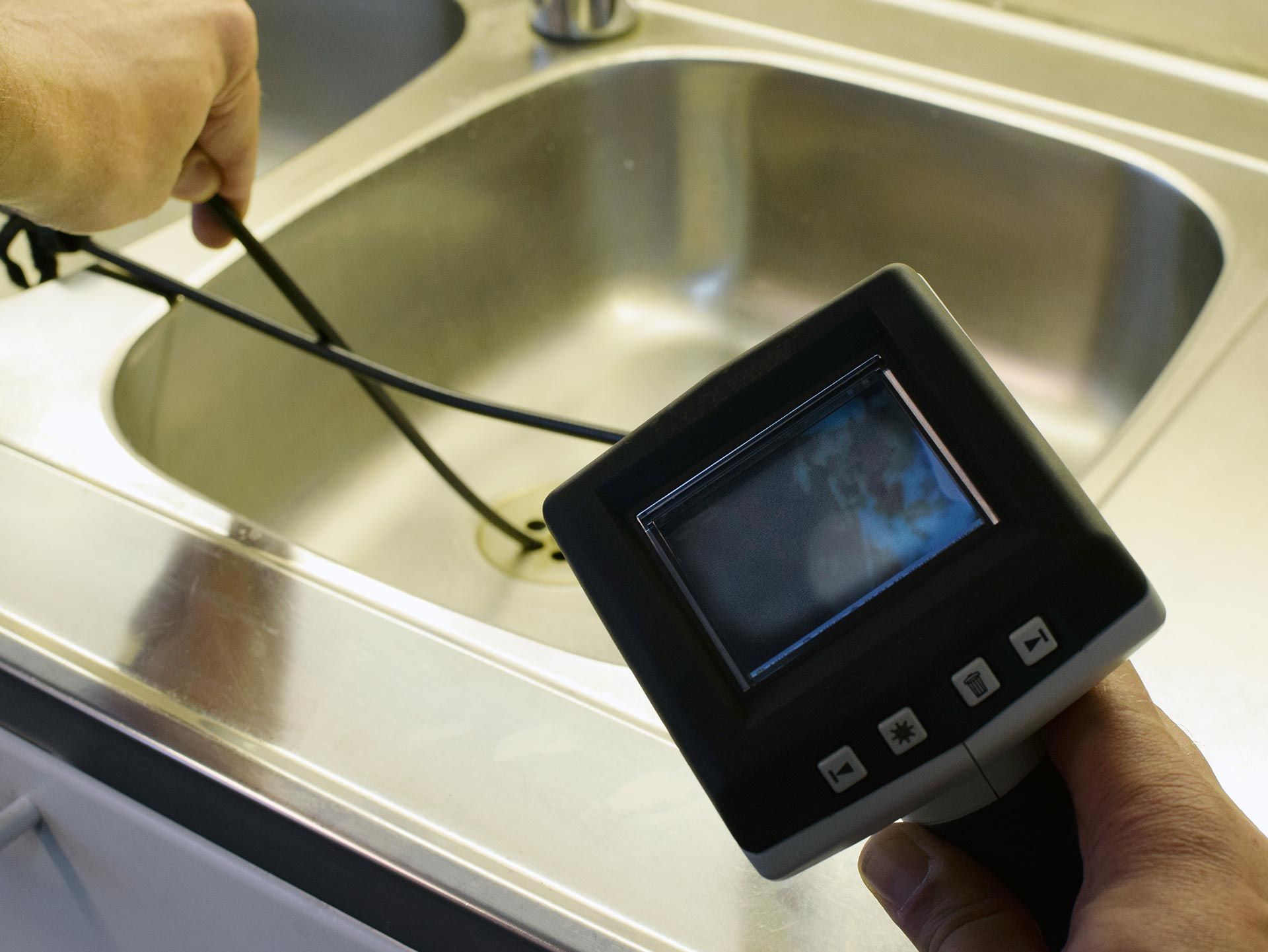 A plumber checking a drain pipe with a borescope inspection camera.