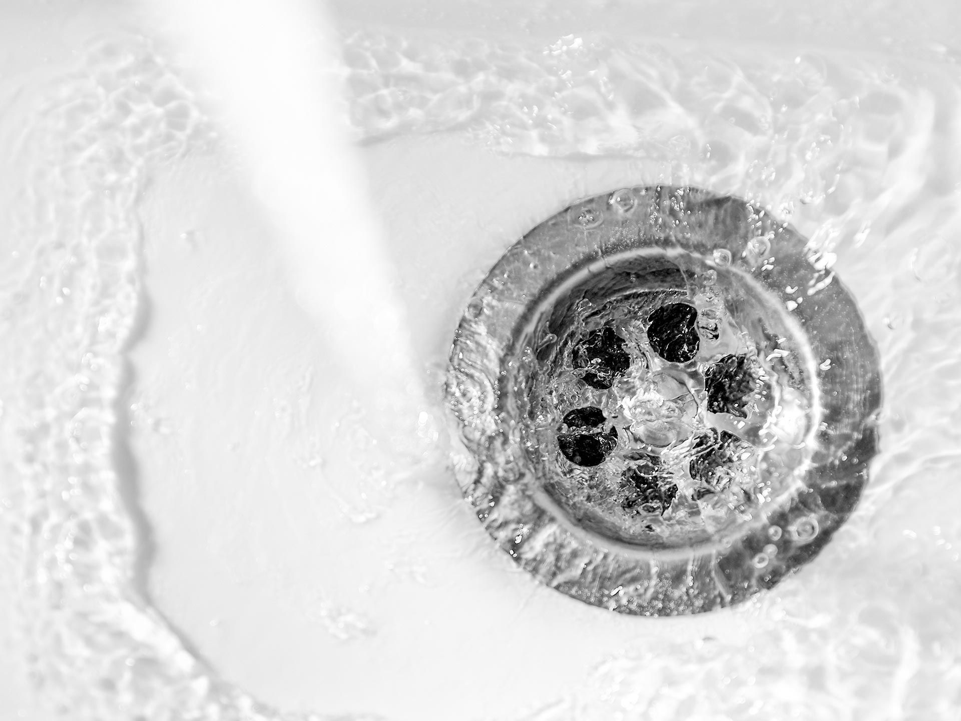A close-up of clear water drains into a drain hole of a white porcelain sink.