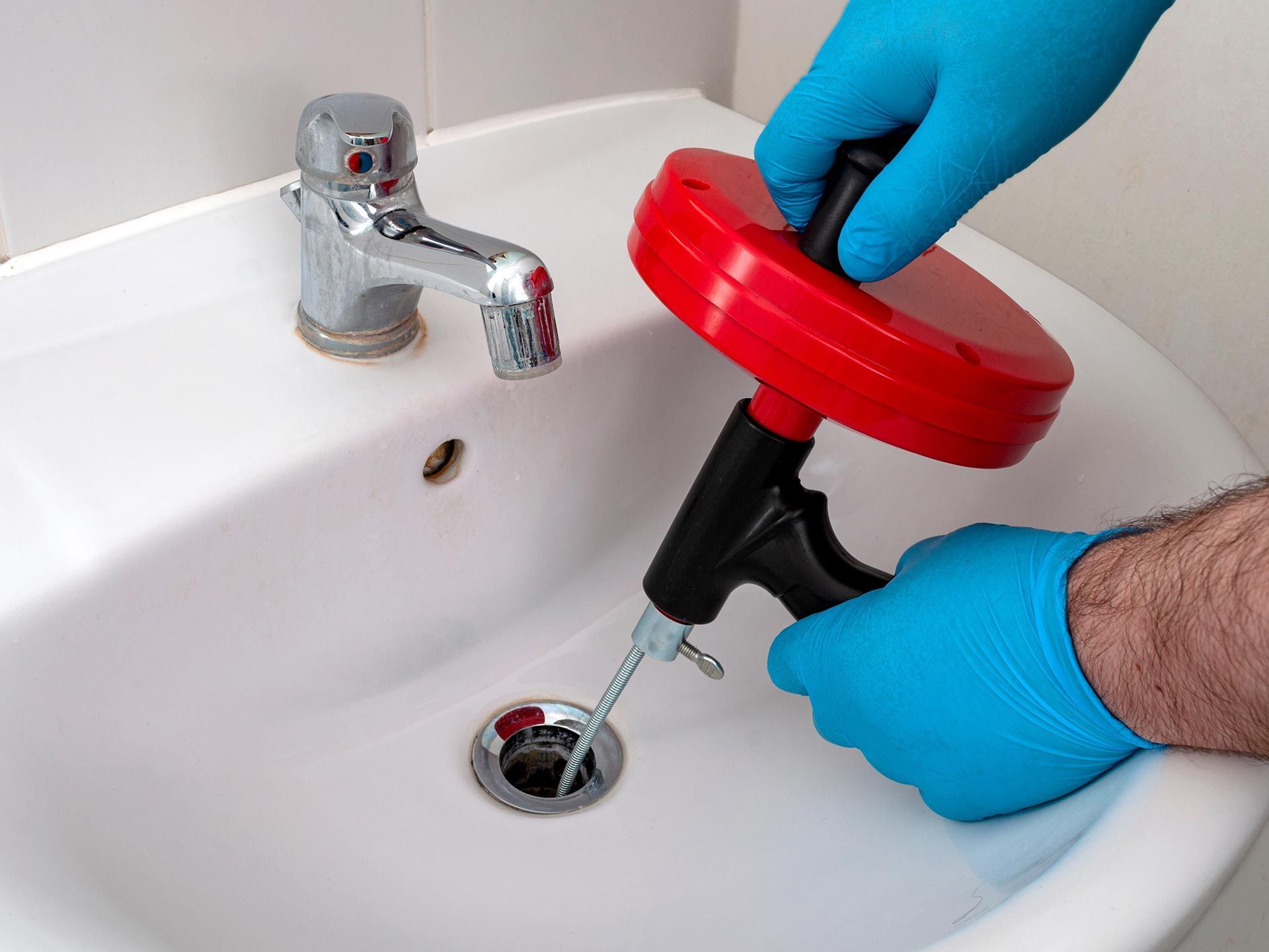 Plumbing contractor cleaning a bathroom drain with a plumber’s snake.
