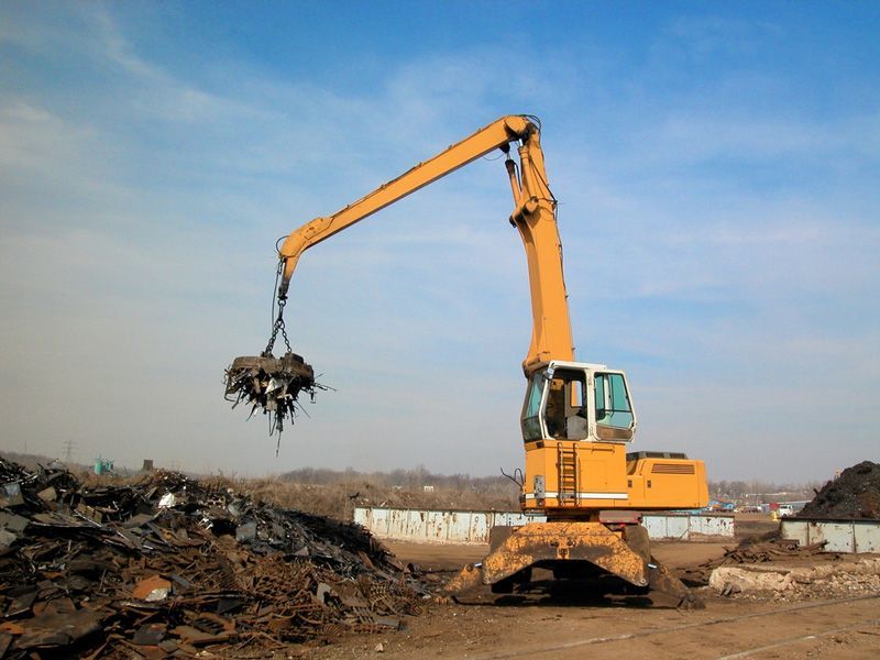 A yellow excavator is loading metal into a pile of scrap metal — Hydro Excavation in Campbelltown, NSW