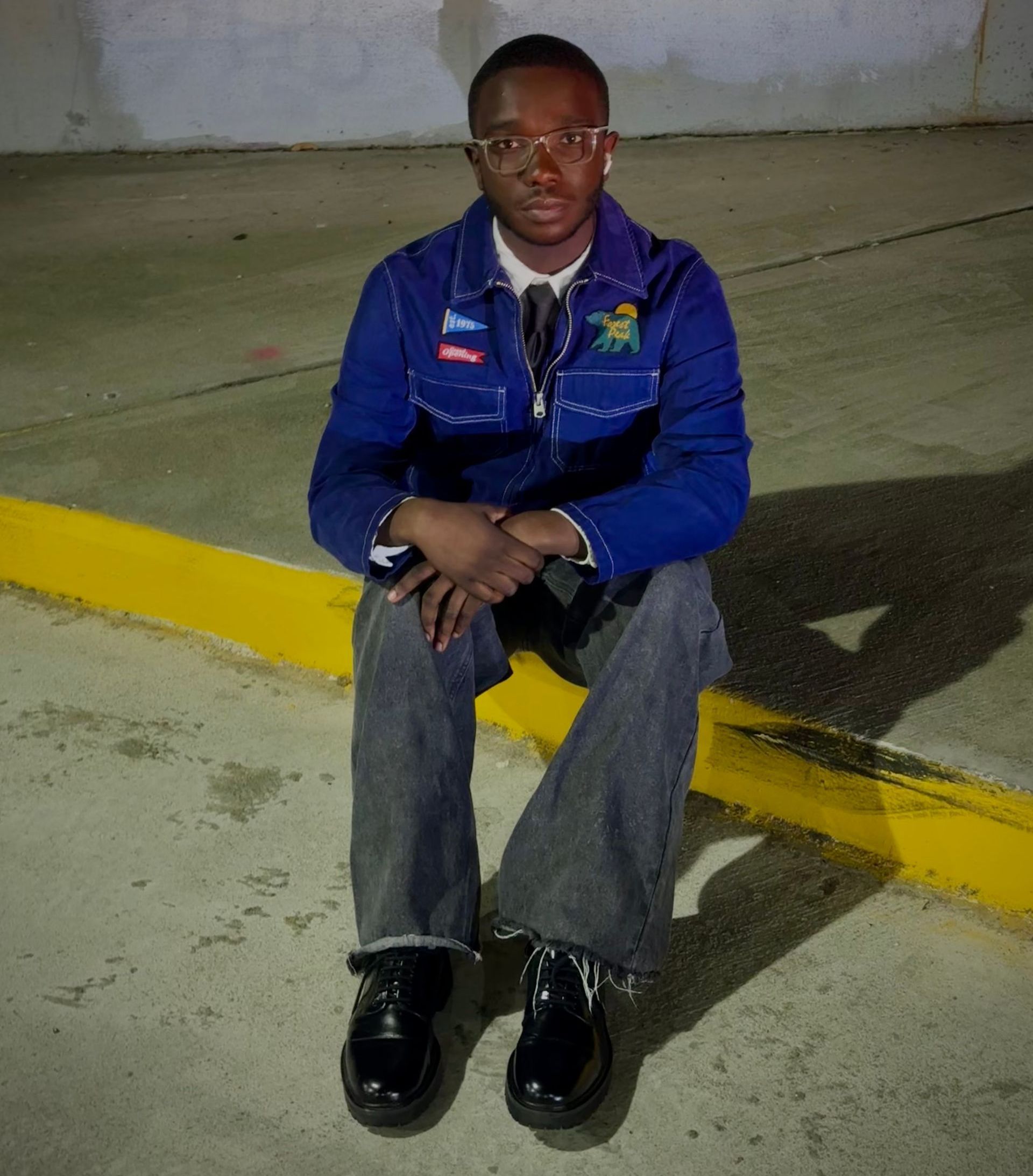 J Cofield in a blue jacket is sitting on a curb