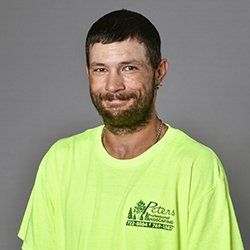 Man in a neon green shirt with a small beard, smiling at the camera. Gray background.