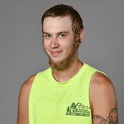 Man with a beard and gauges in a yellow tank top smiles.
