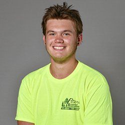 Smiling young man in neon yellow shirt; gray background.