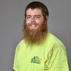 Man with a long, reddish-brown beard, wearing a green shirt; he's smiling and the shirt has a landscaping logo.