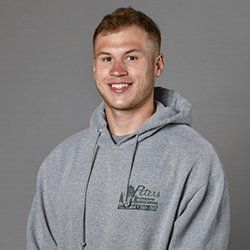 Man in gray hoodie smiles, logo on front.