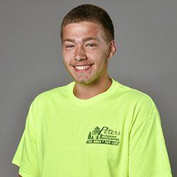 A young man with fair skin, wearing a neon green t-shirt with the company logo, smiles at the camera.