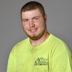 Man in a yellow shirt smiles at the camera. He has a beard and short brown hair. Gray background.