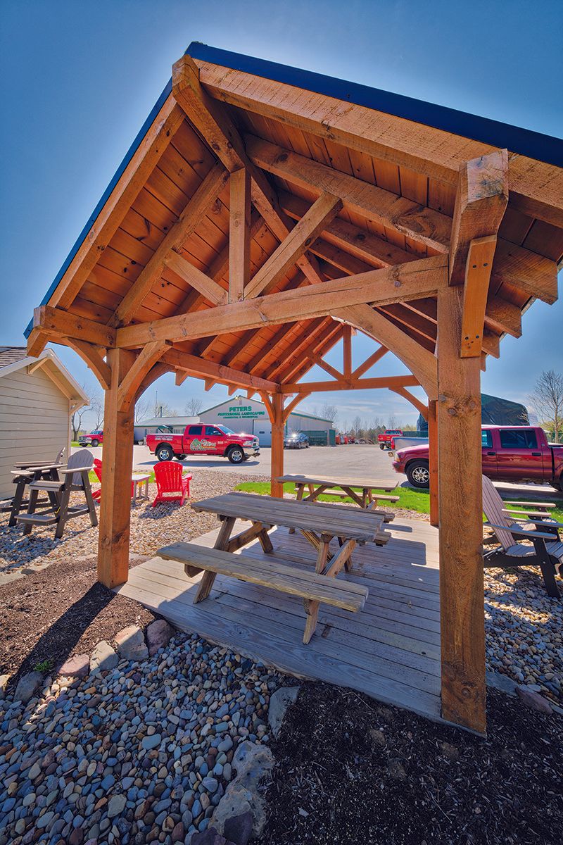 Wooden pavilion with picnic tables. Red truck in background under blue sky.