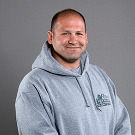 Man in gray hooded sweatshirt smiles at camera.
