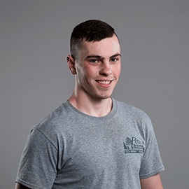 Man with short brown hair smiles at the camera, wearing a gray t-shirt. Gray background.