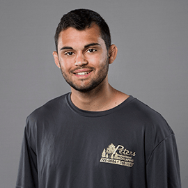 Man with a short beard, wearing a gray t-shirt with a company logo, smiling at the camera.