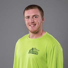 Man wearing a neon green shirt smiling, logo on chest, gray background.