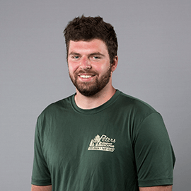 A smiling man with a beard wearing a green shirt with a company logo against a gray background.