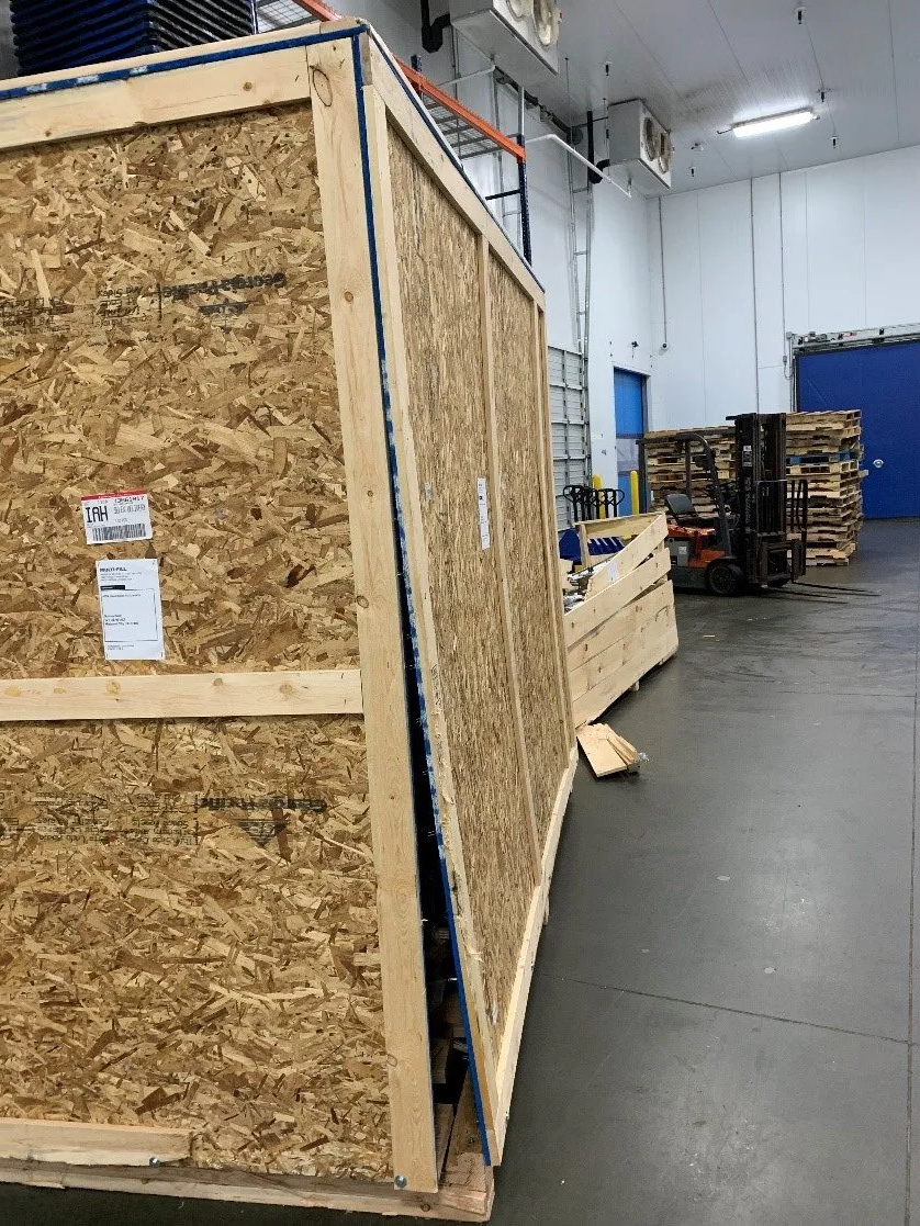 A large wooden crate is sitting in a warehouse next to a forklift.