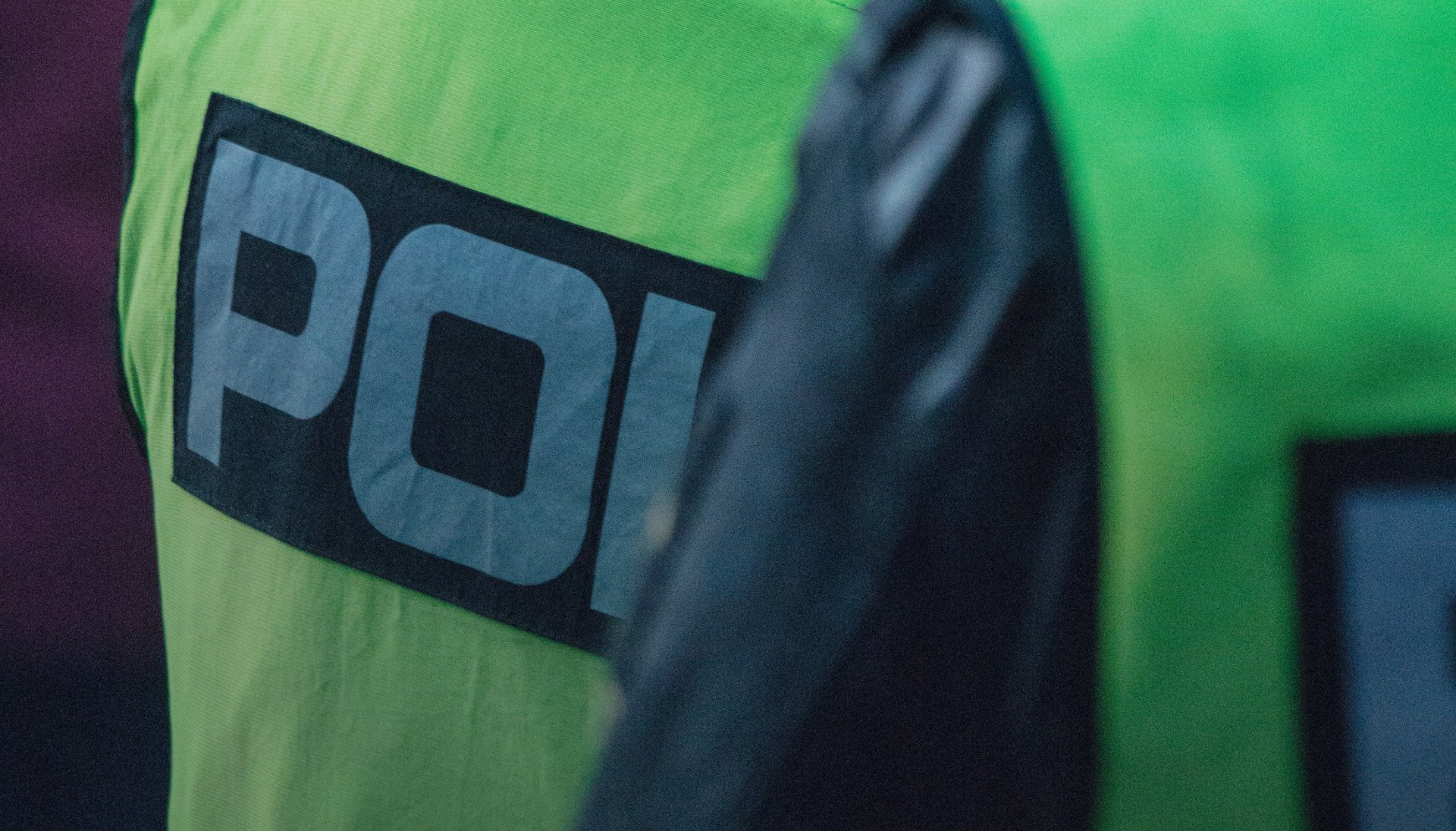 A close up of a person wearing a green vest with the word police on it.