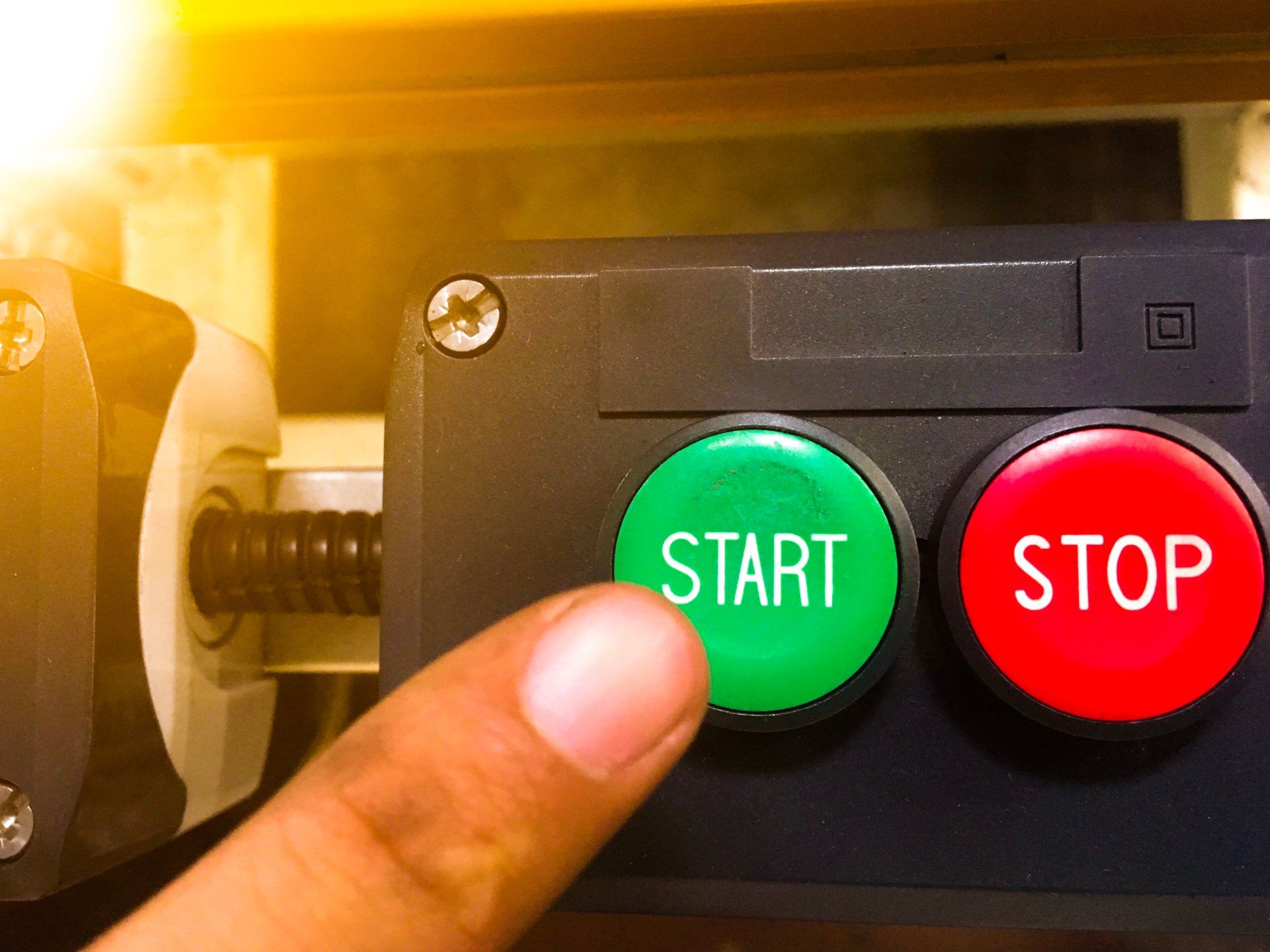 A person is pressing a green start button next to a red stop button.