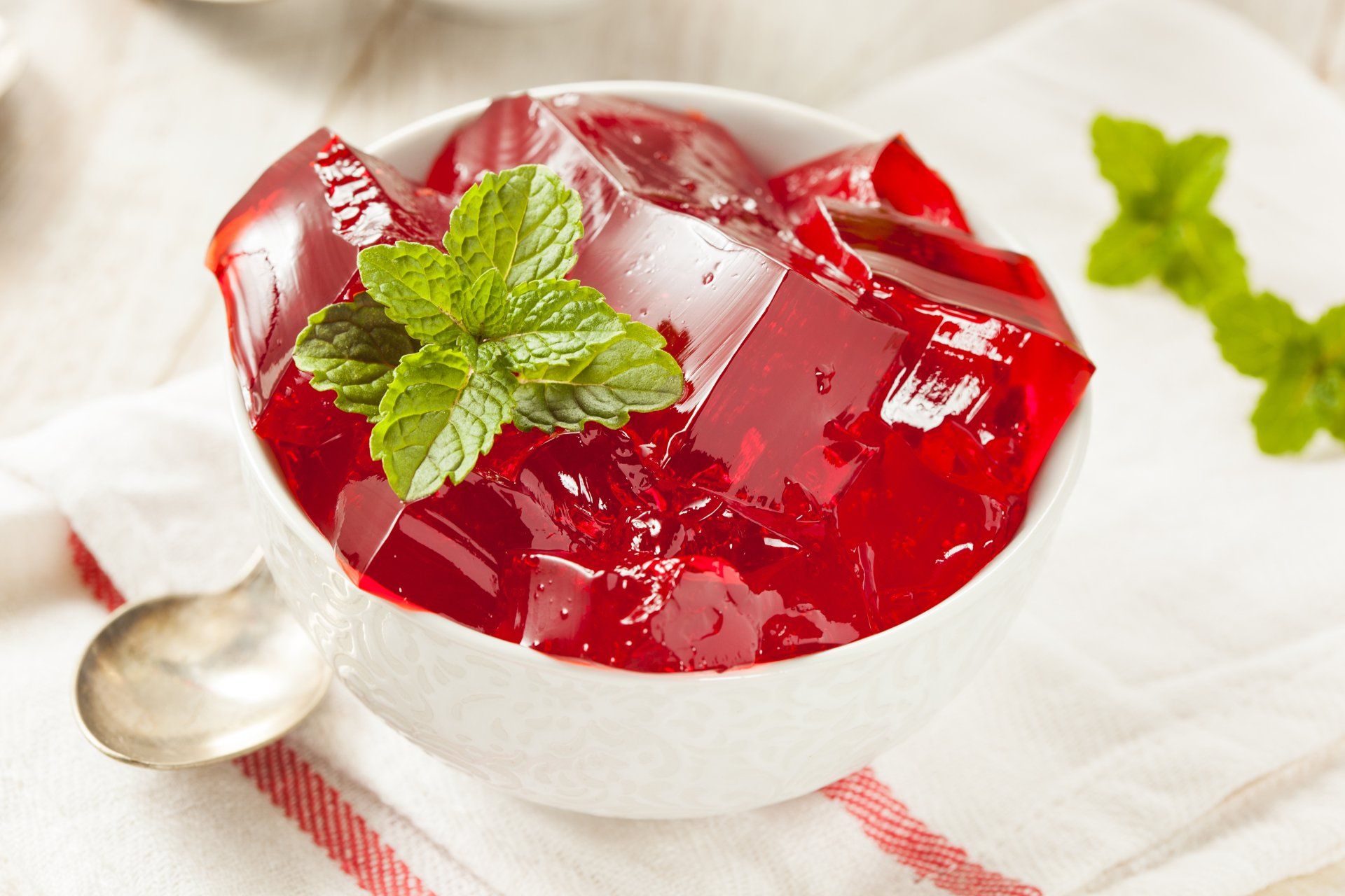 A bowl of red jelly with mint leaves and a spoon.