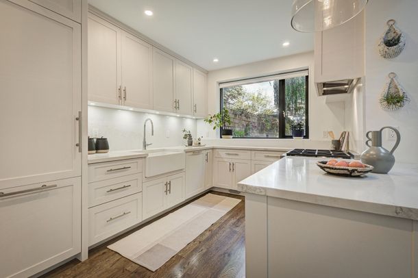 A kitchen with white cabinets , a sink , a stove and a window.