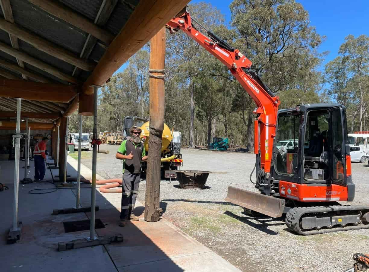 A Man Is Standing Next To A Red Excavator In A Parking Lot — East Coast Locating Services In Lake Macquarie, NSW