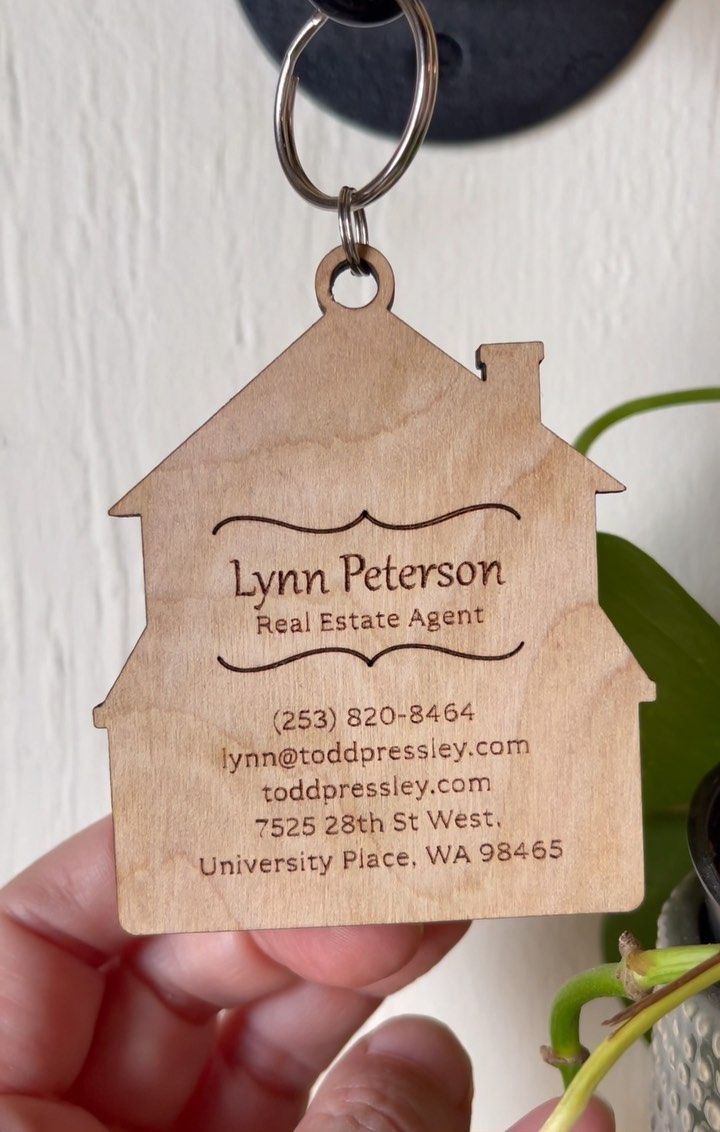 A person is holding a wooden keychain that says lynn peterson real estate agent