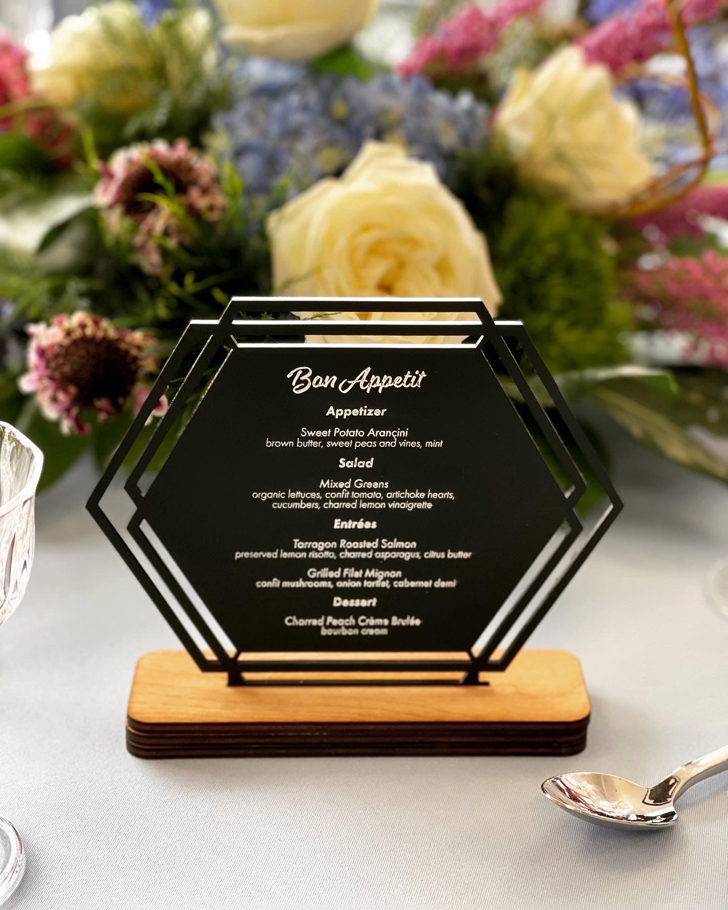 A menu is sitting on a table next to a spoon and flowers.