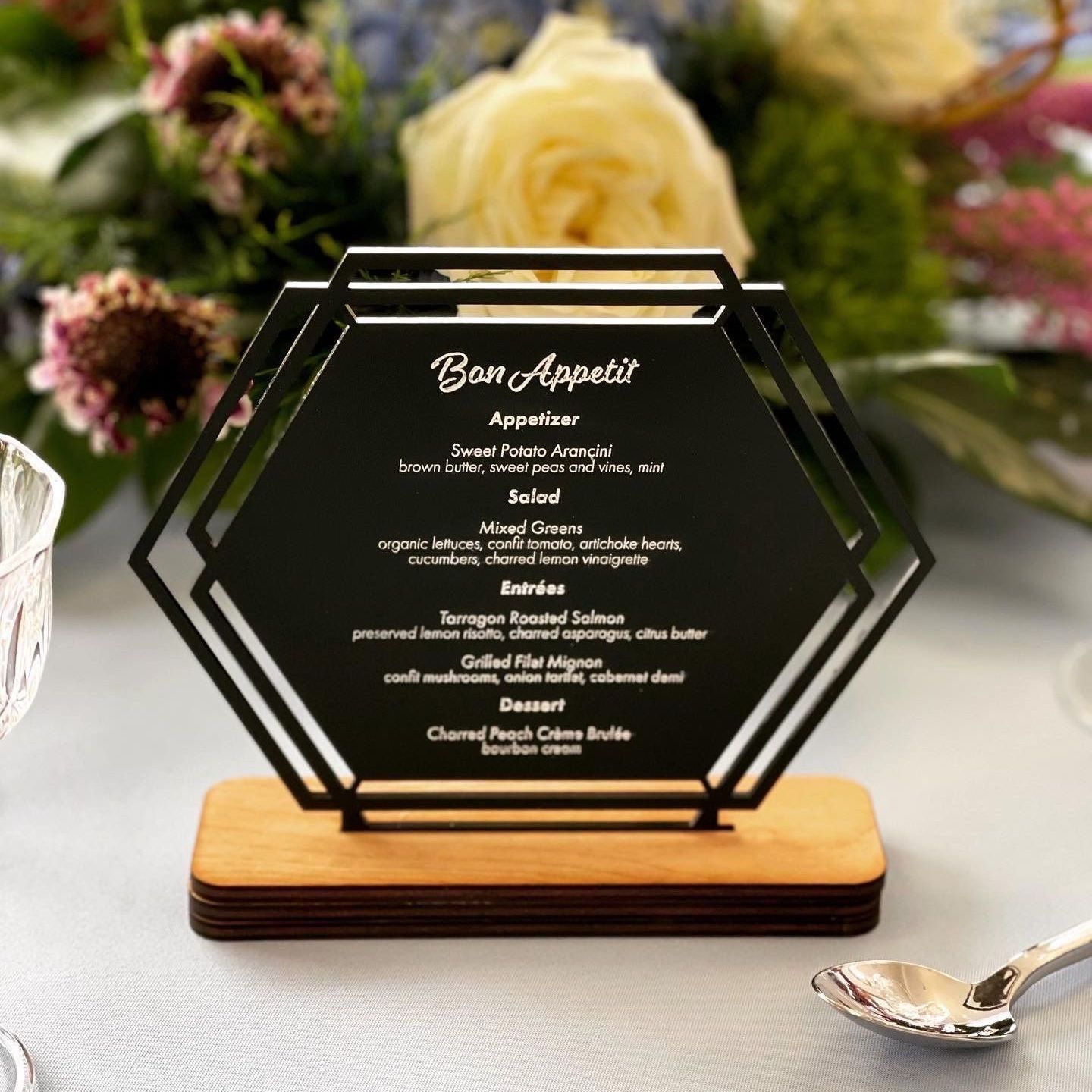 A menu is sitting on a table next to a spoon and flowers.