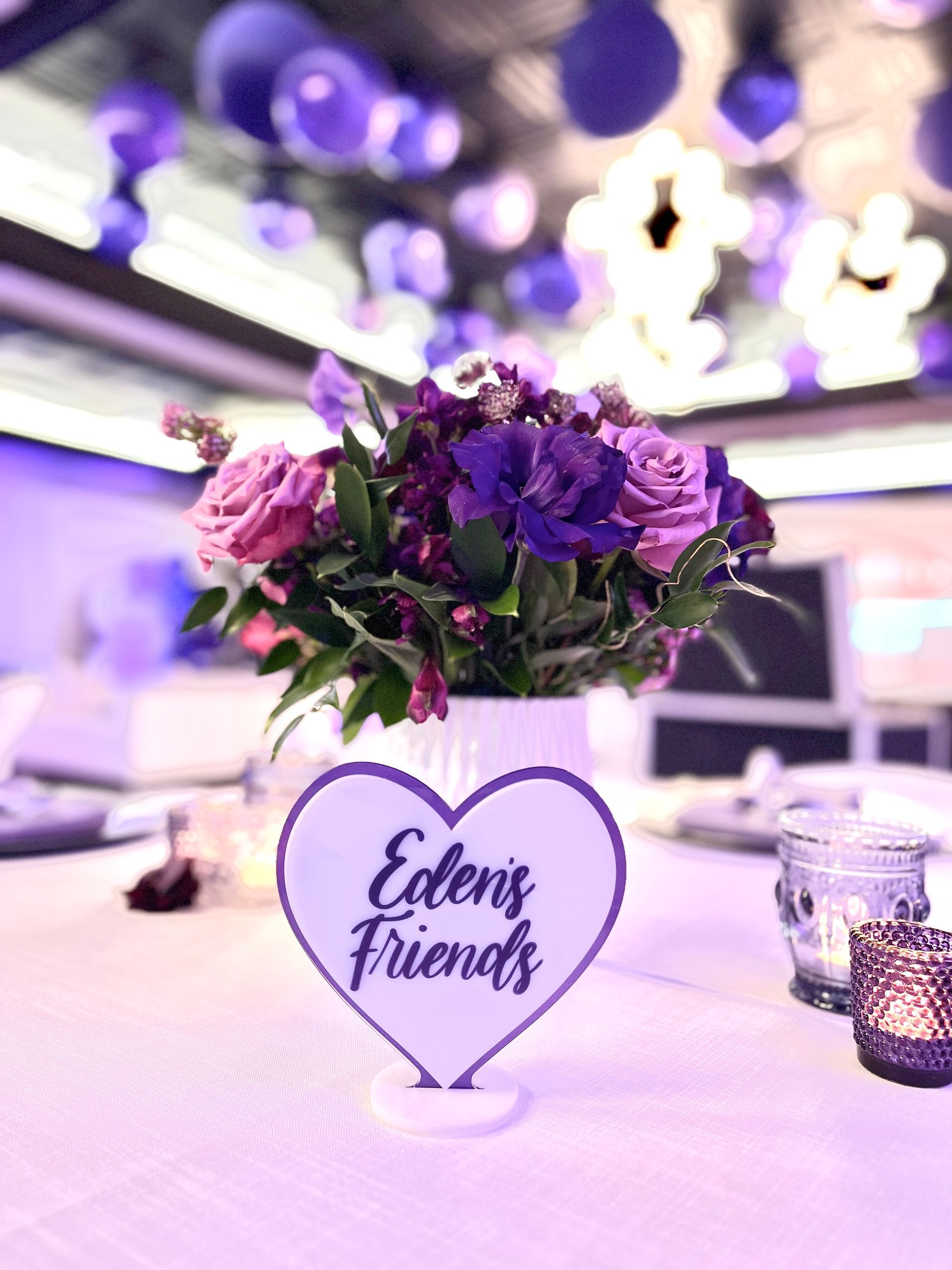 A heart shaped vase filled with purple flowers and a sign that says eden 's friends