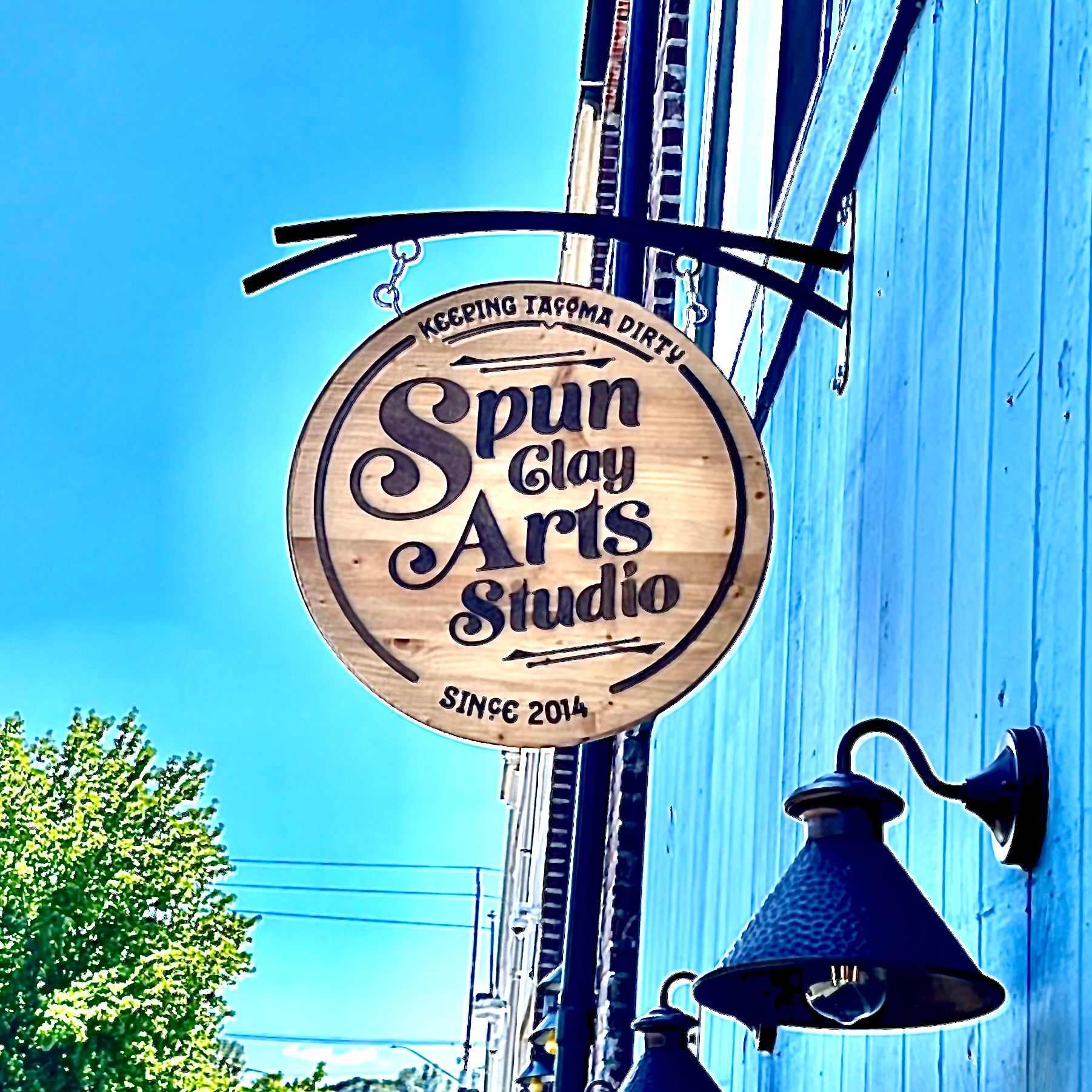 A sign for spun clay arts studio hangs on a blue building
