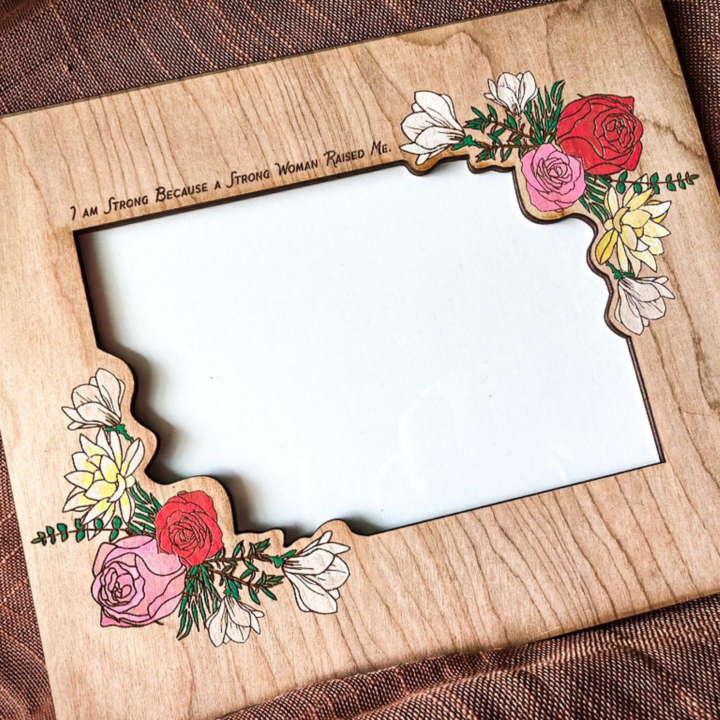 A wooden picture frame with flowers on it is sitting on a table.