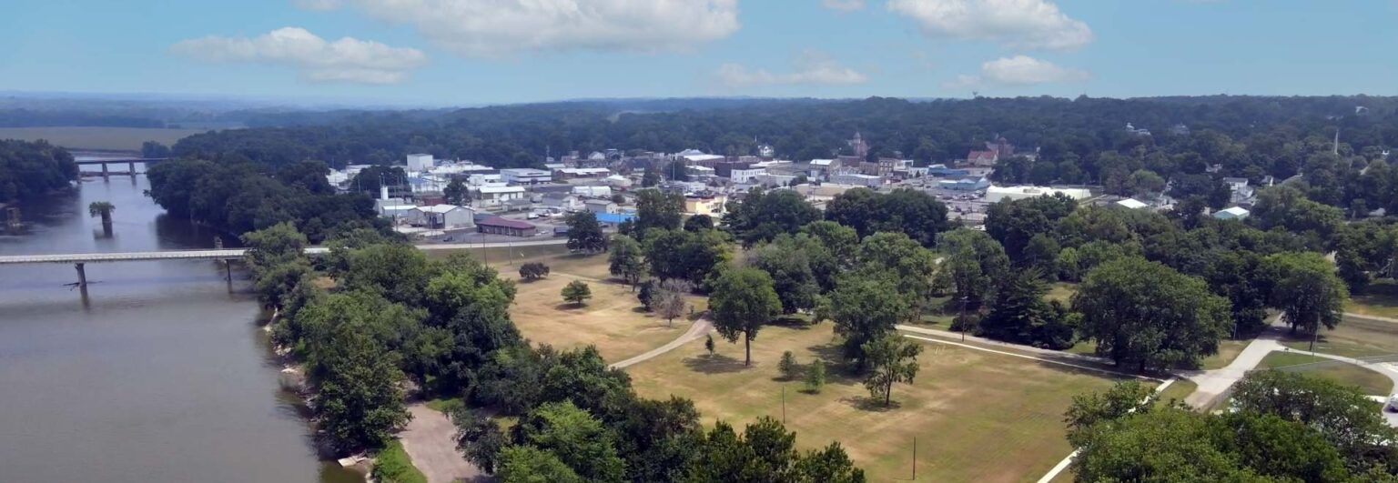 Aerial view of a small town surrounded by trees and a river with two bridges.