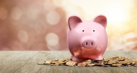 A pink piggy bank is sitting on top of a pile of coins.