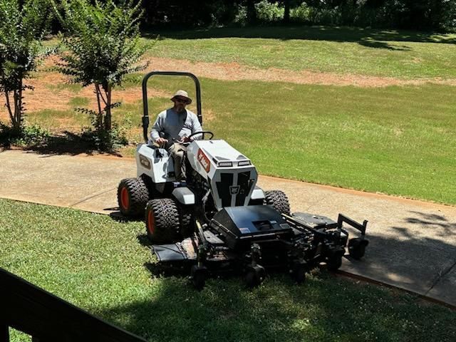 A man is riding a lawn mower down a sidewalk.