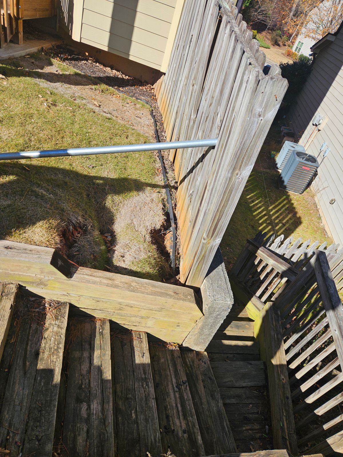 A wooden staircase leading up to a house with a fence in the background.