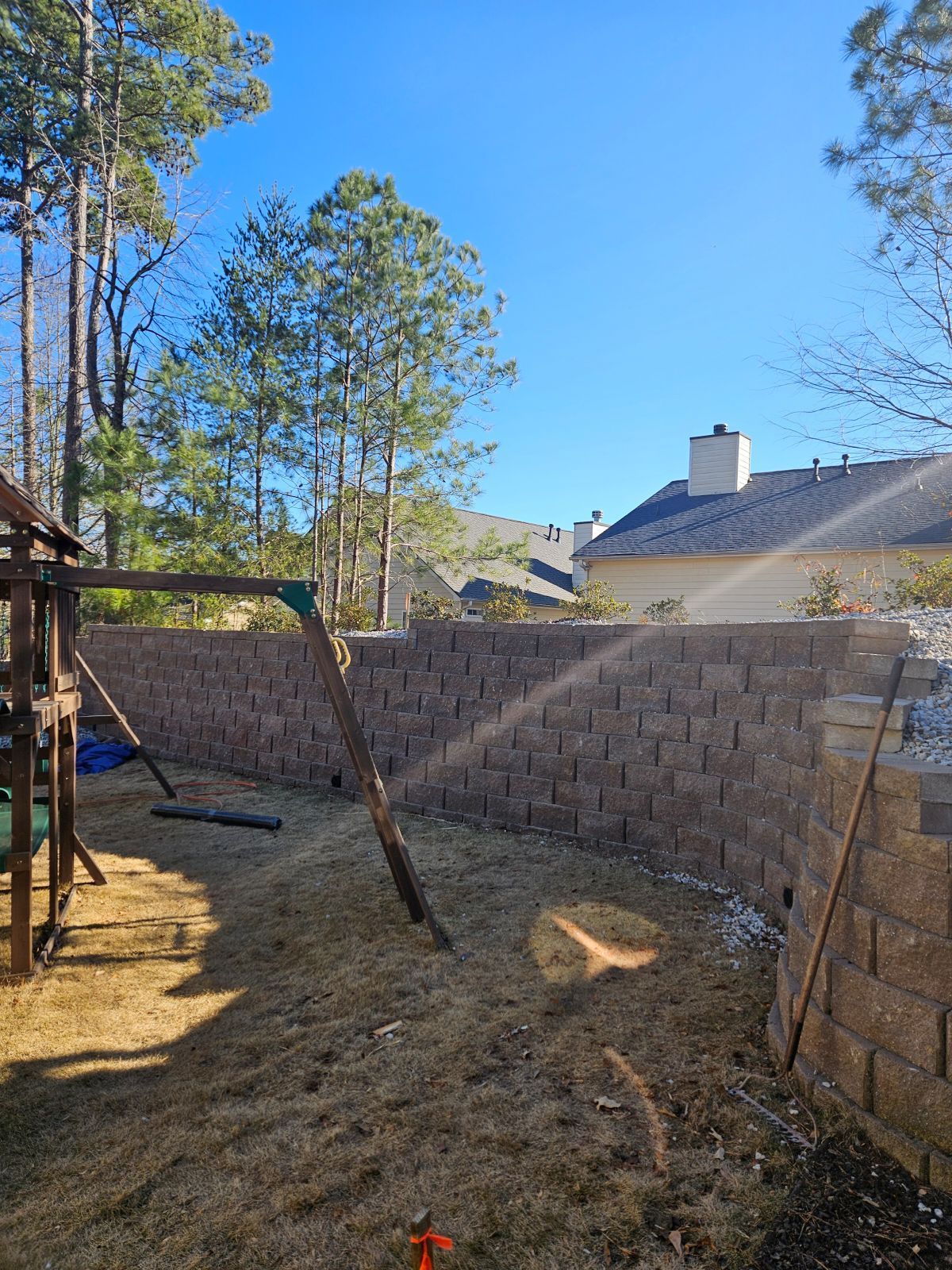 A backyard with a swing set and a brick wall.