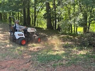 A man is riding a lawn mower on a dirt road in the woods.