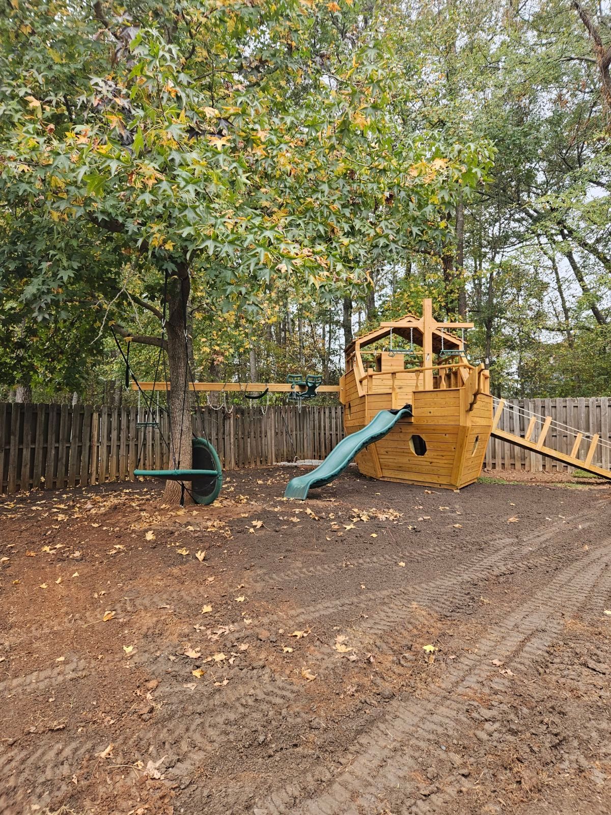A wooden playground in the shape of a ship with a slide and swings.