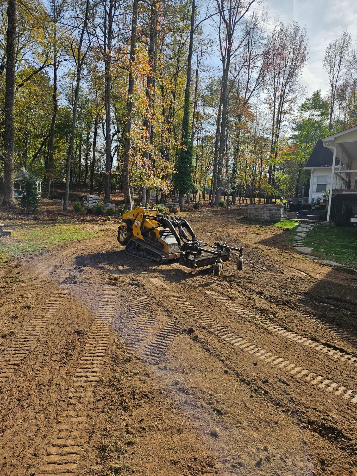 A yellow tractor is driving down a dirt road in front of a house.