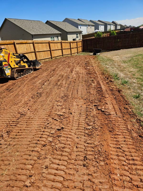 A bulldozer is driving down a dirt road next to a wooden fence.
