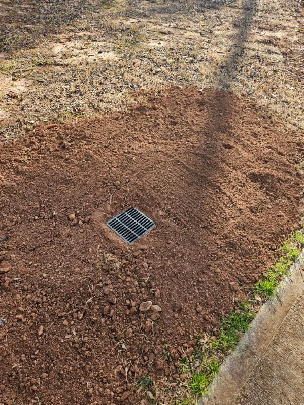 A drain hole in the ground next to a sidewalk.