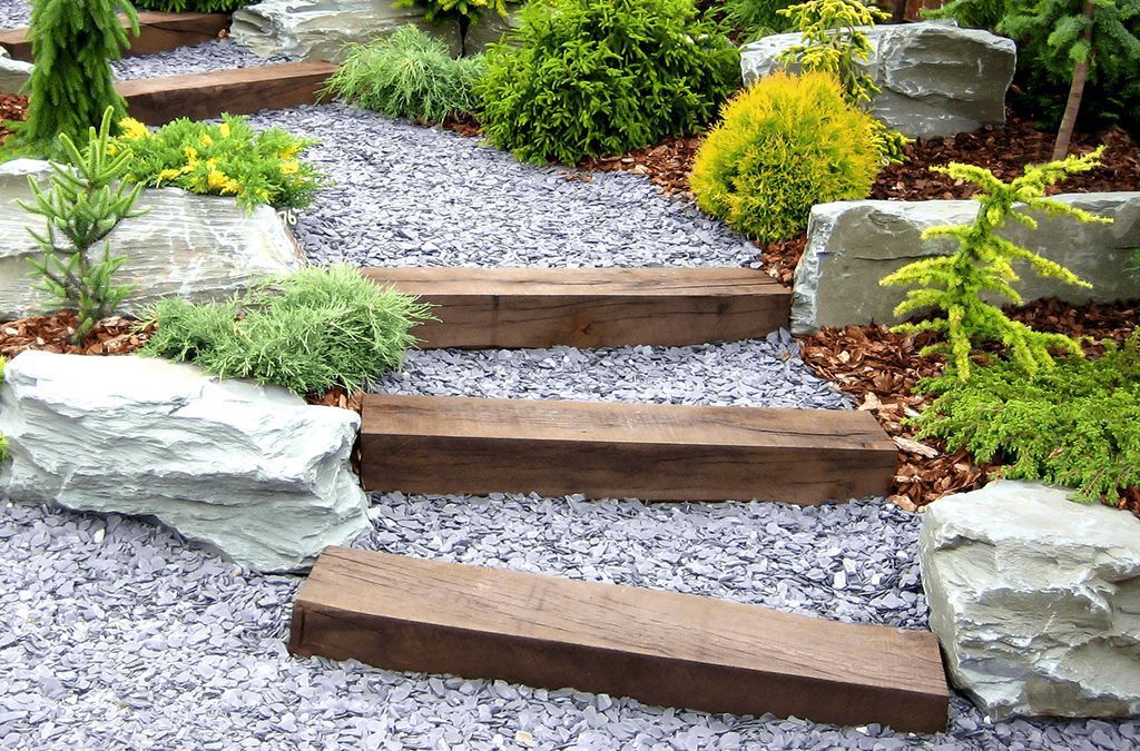 A wooden staircase in a garden surrounded by rocks and plants.