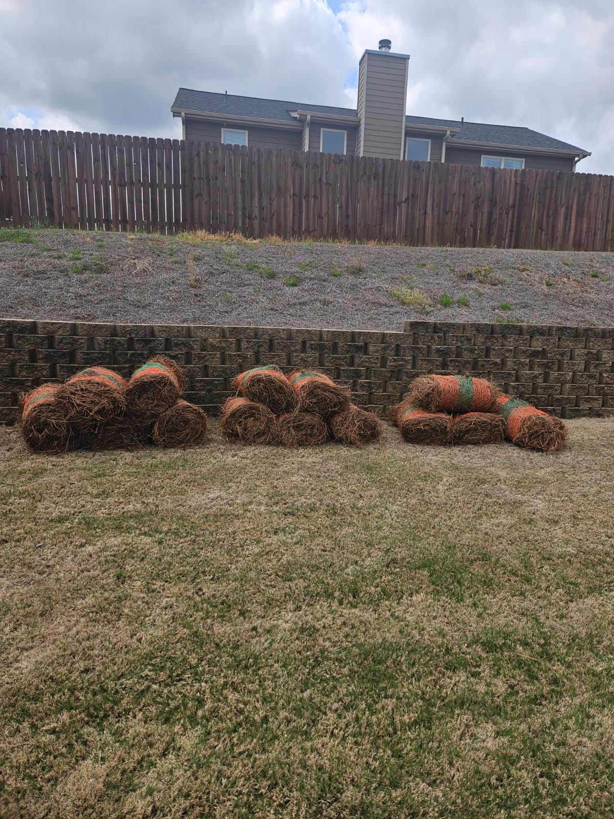 A bunch of hay bales sitting on top of a lush green lawn in front of a house.