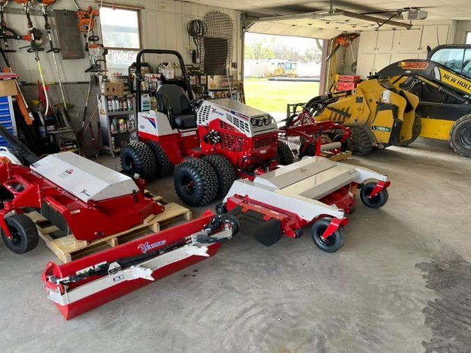 A bunch of lawn mowers are parked in a garage.
