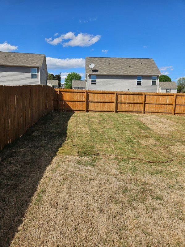 A backyard with a wooden fence and a house in the background.