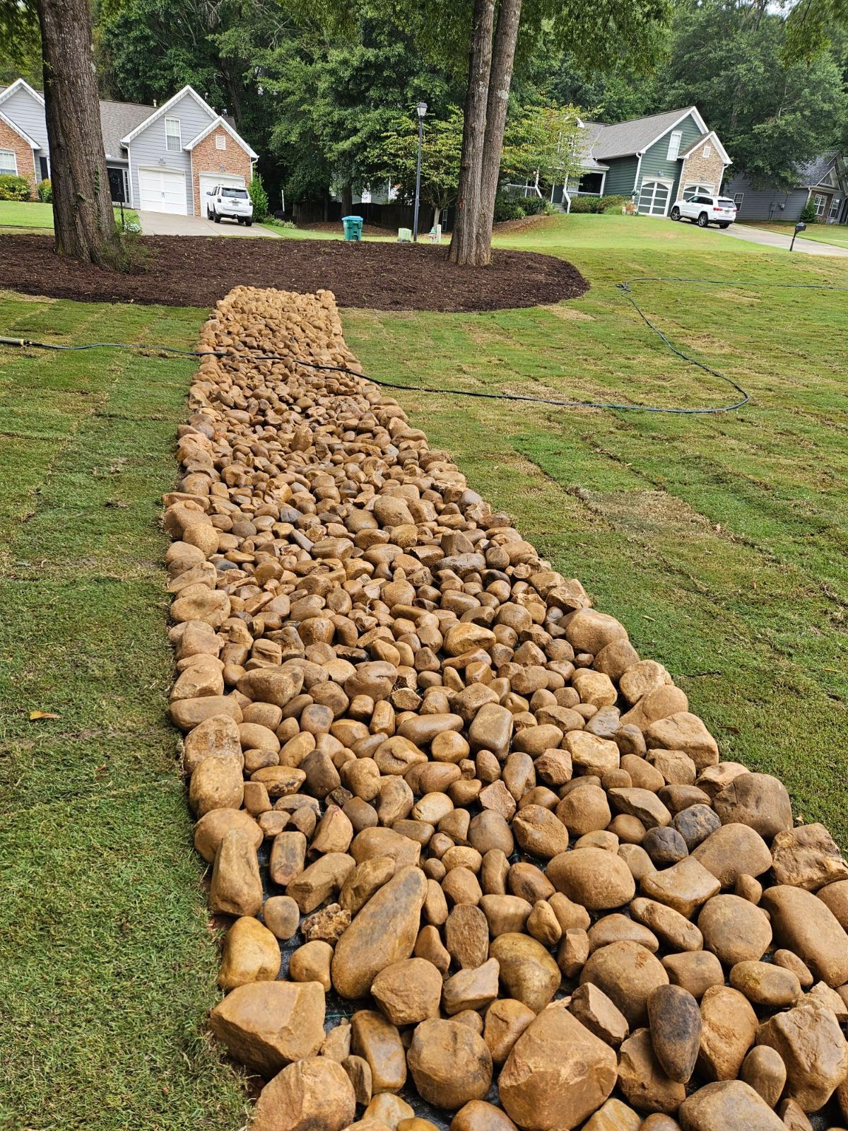 A path made of river rocks in the middle of a lush green field.