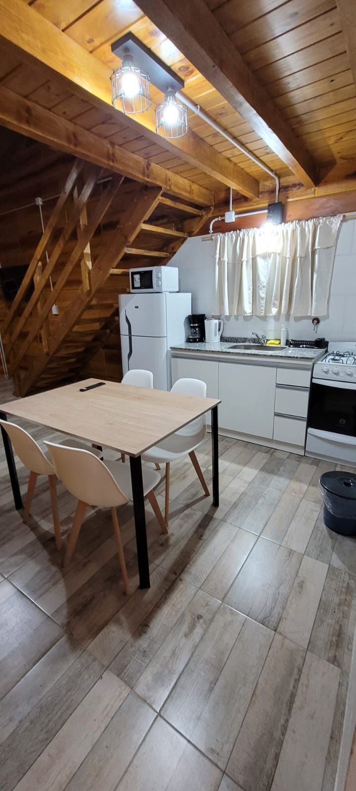 Una acogedora cocina y comedor con techos de madera y escalera. Hay una mesa con sillas, un refrigerador y una estufa. Cabaña Los Ciruelos