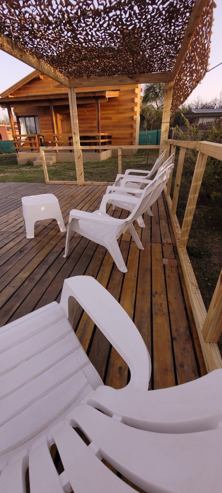 Cabaña de madera con terraza con sillas blancas bajo un dosel; el entorno sugiere un espacio relajante al aire libre. Cabaña Los Ciruelos