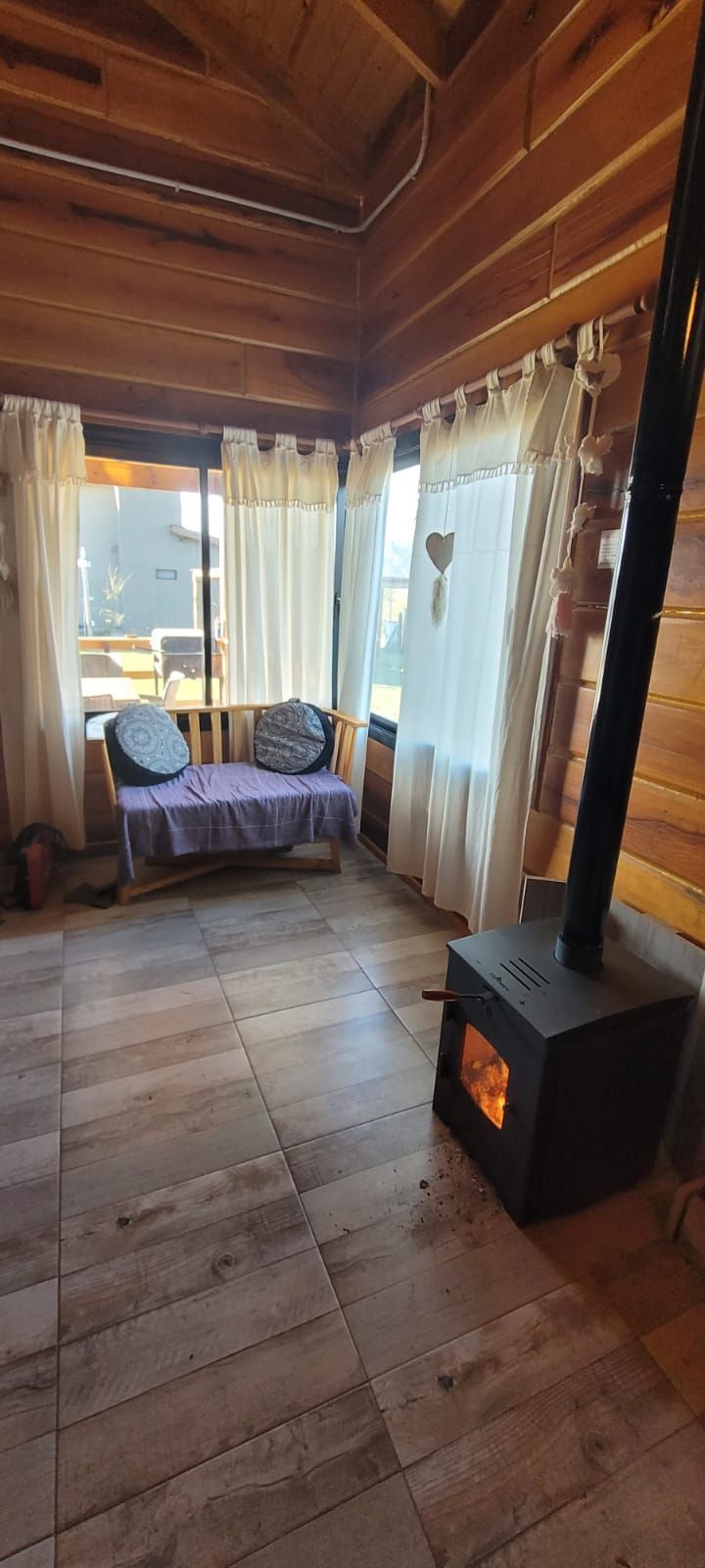 Acogedor interior de cabaña con estufa de leña, paredes de madera y una pequeña zona de estar junto a una ventana. Cabaña Los Ciruelos