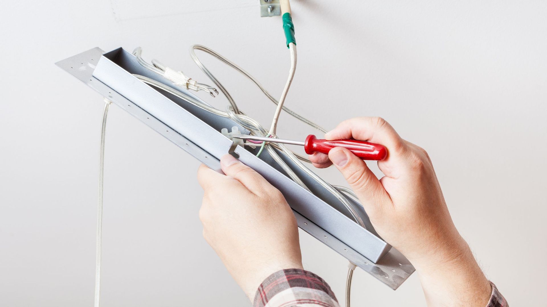 A person is fixing a light fixture with a screwdriver.